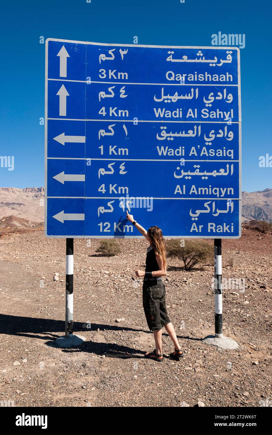 Una mujer señala una señal de tráfico escrita en árabe en las montañas de Omán Foto de stock