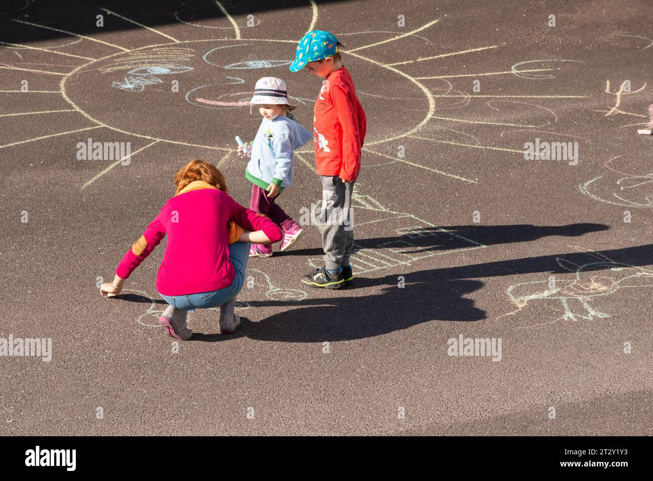 Madre jugando con niños dibujando figuras con tiza en el patio de recreo de asfalto como actividad al aire libre familiar Foto de stock