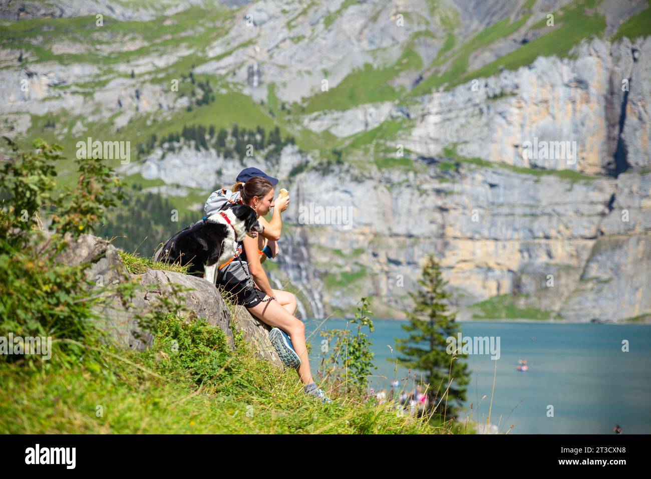 Lago Oeschinen, Suiza–Agosto de 3,2023: Una niña blanca con perro descansando sobre las rocas en los Alpes con la montaña al fondo Foto de stock