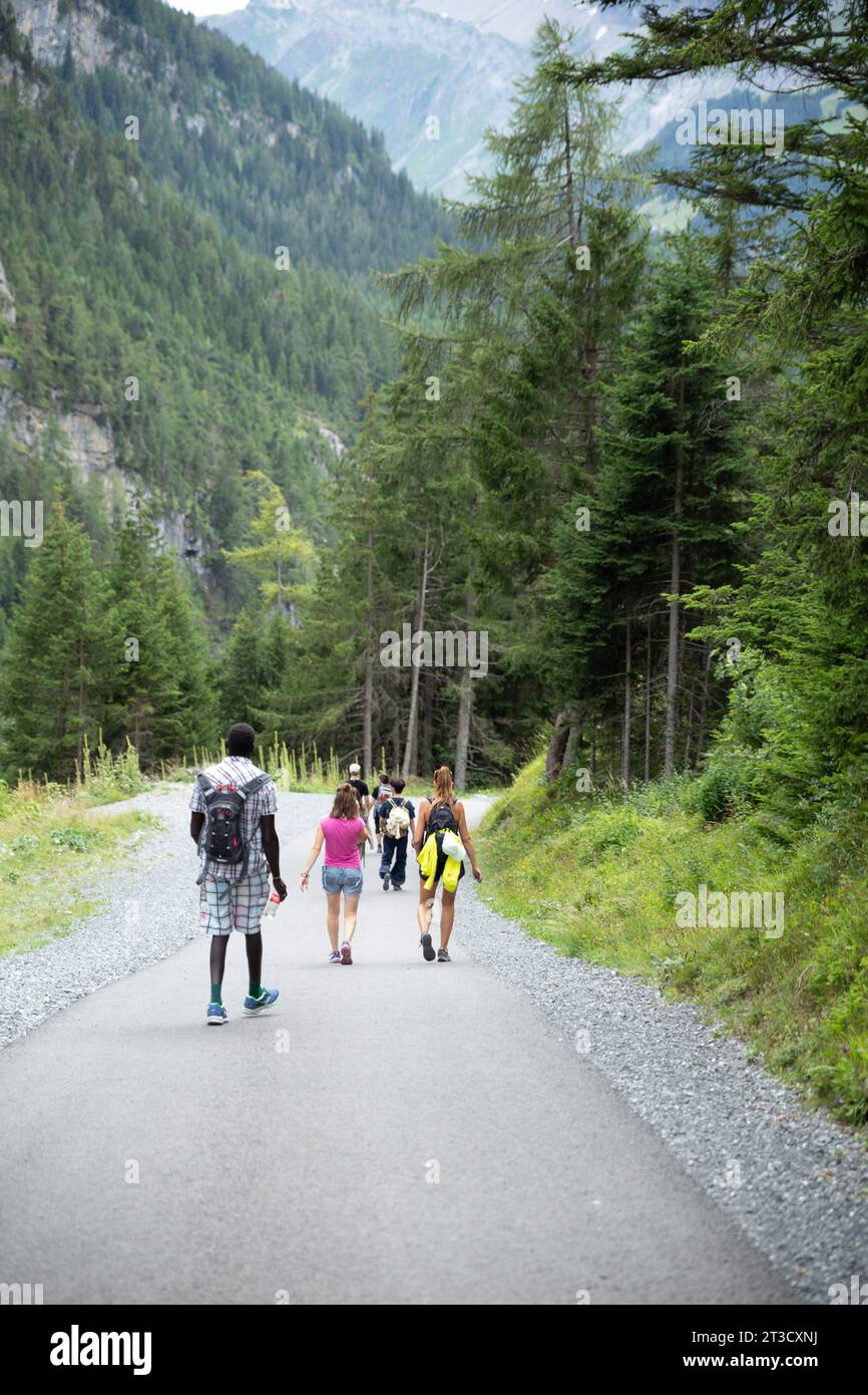 Kandersteg, Suiza–agosto de 3,2023: Turistas que caminan por un camino con bosque de pinos y montañas en los Alpes Foto de stock