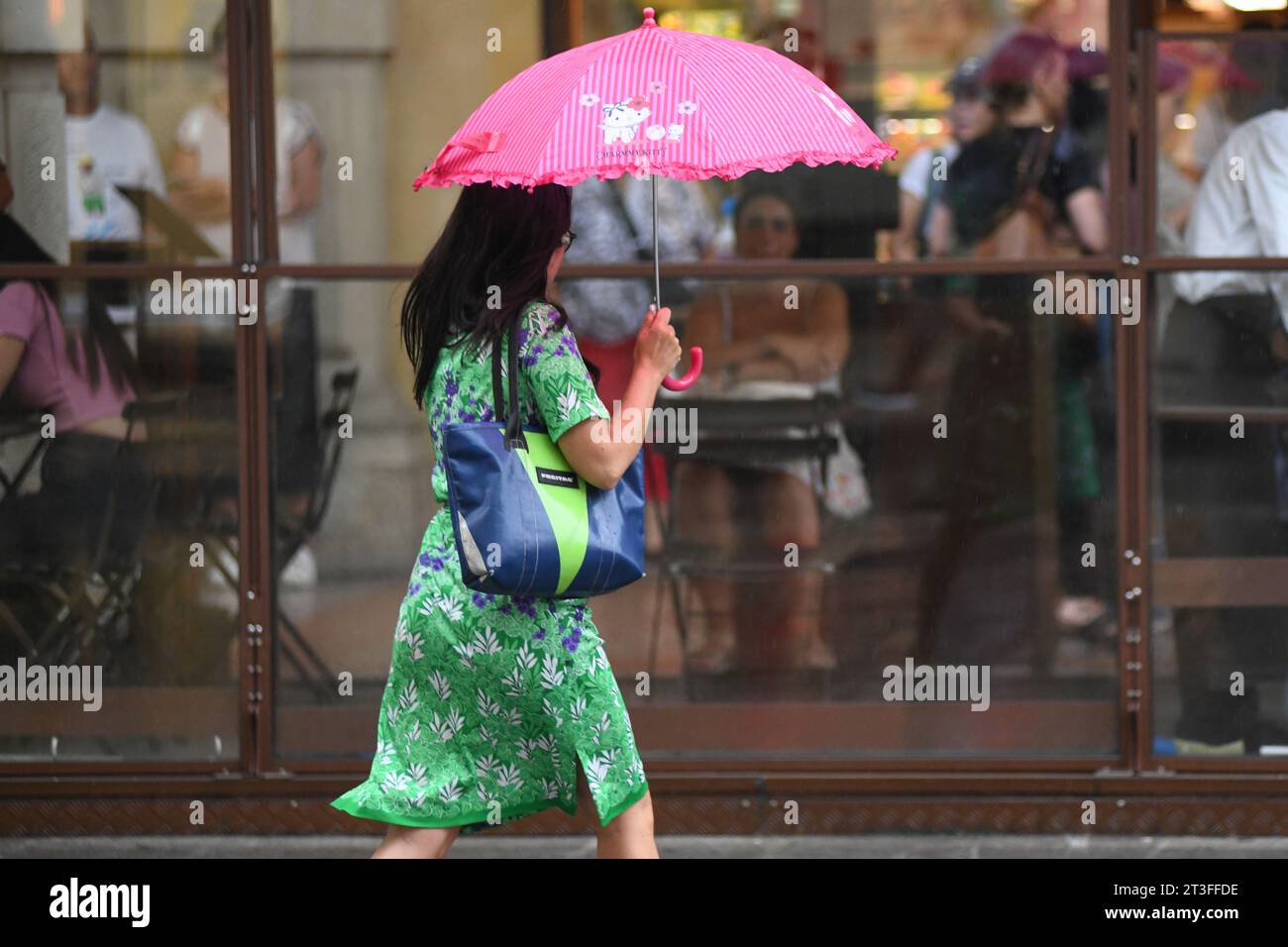 Mujer que cruza la calle bajo la lluvia con un paraguas. Via Ugo Bassi, Bolonia, Italia. Foto de stock