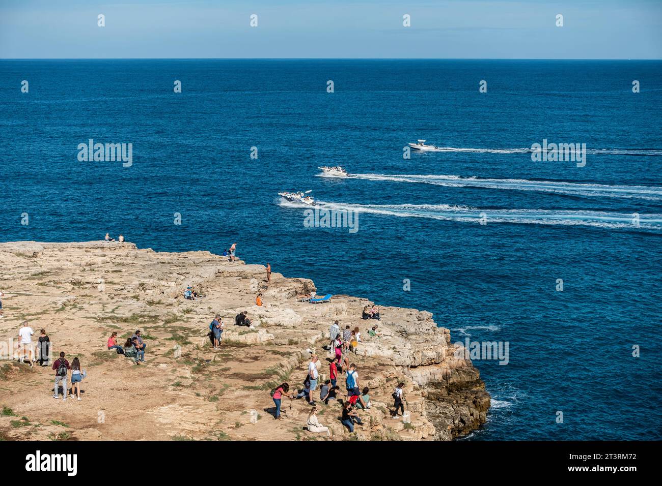 Gente disfrutando del tiempo soleado en el afloramiento rocoso frente a la playa de Cala Ponte en Polignano a Mare, Italia, Foto de stock