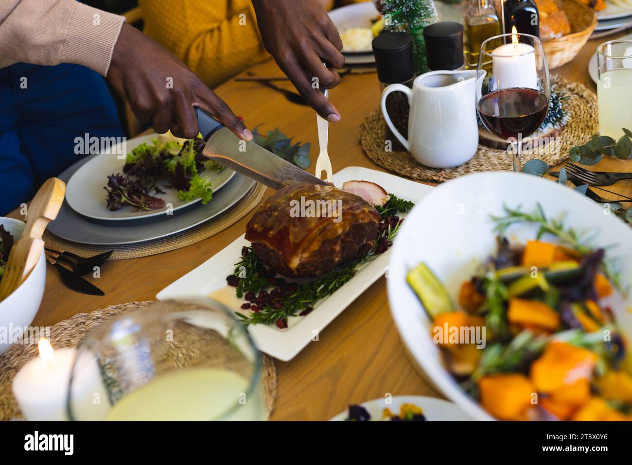 Hombre afroamericano cortando carne en la cena familiar de navidad en el comedor decorado en casa Foto de stock