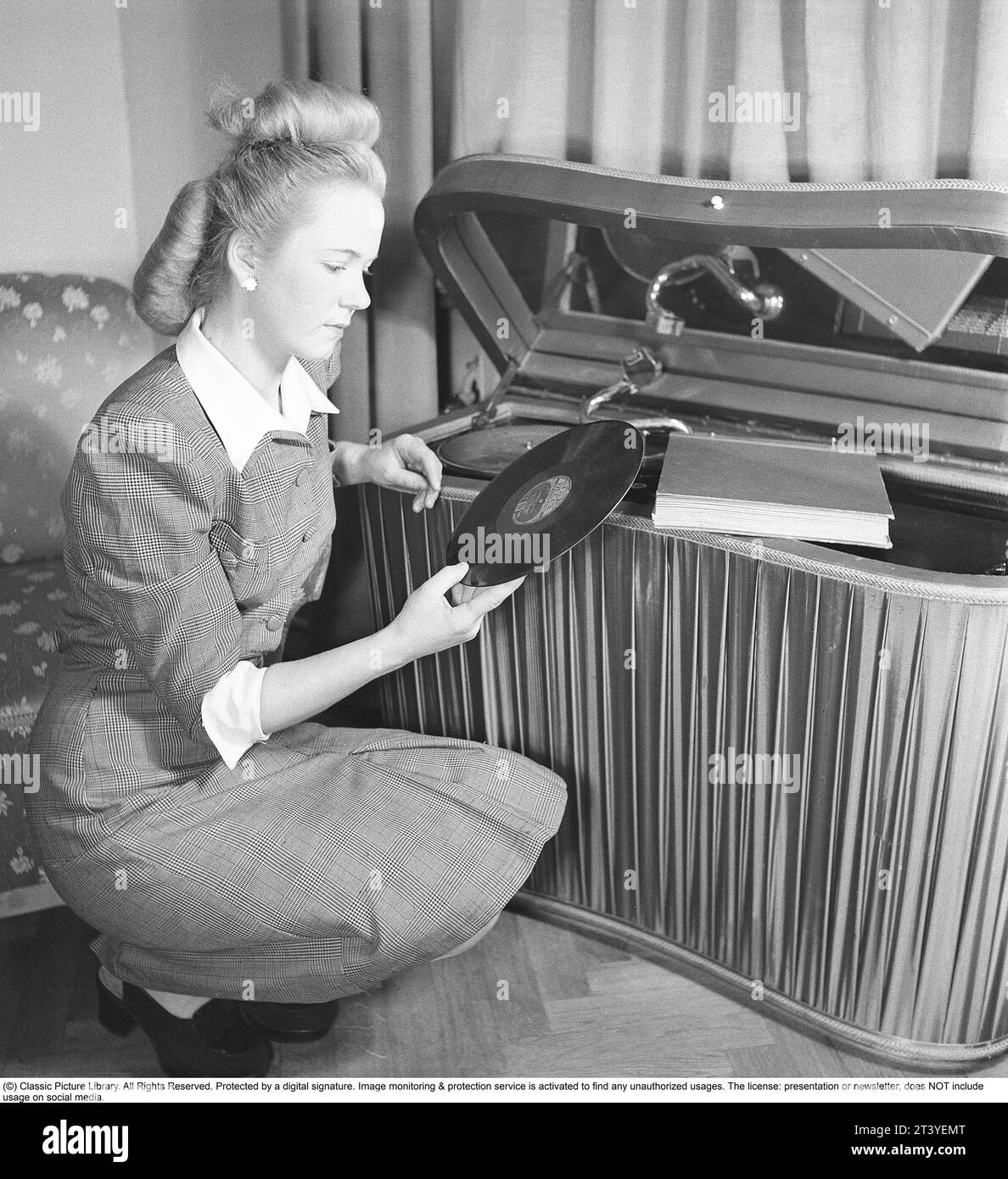 Mujer en un gramófono en los años cuarenta. Tiene uno de los discos para leer la etiqueta que contenía la información sobre lo que se grabó, el nombre de las canciones y el artista. Generalmente el logotipo de la compañía discográfica fue presentado en la etiqueta. Los discos estaban hechos de material frágil y la velocidad del disco para sonar como debería era de 78 revoluciones por minuto. El gramófono es un modelo de lujo con una tela de satén que cubre los laterales. Suecia 1947. Kristoffersson ref AB22-4 Foto de stock