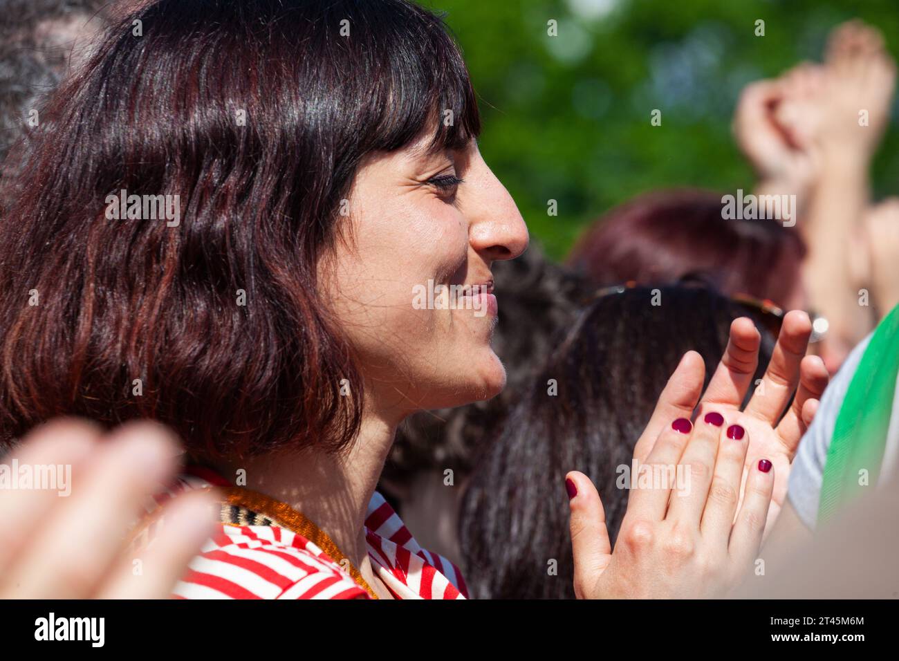 Gattatico, Reggio Emilia, Italia - 25 de abril de 2023: Vista lateral de la mujer joven aplaudiendo manos viendo concierto en el parque al aire libre Foto de stock