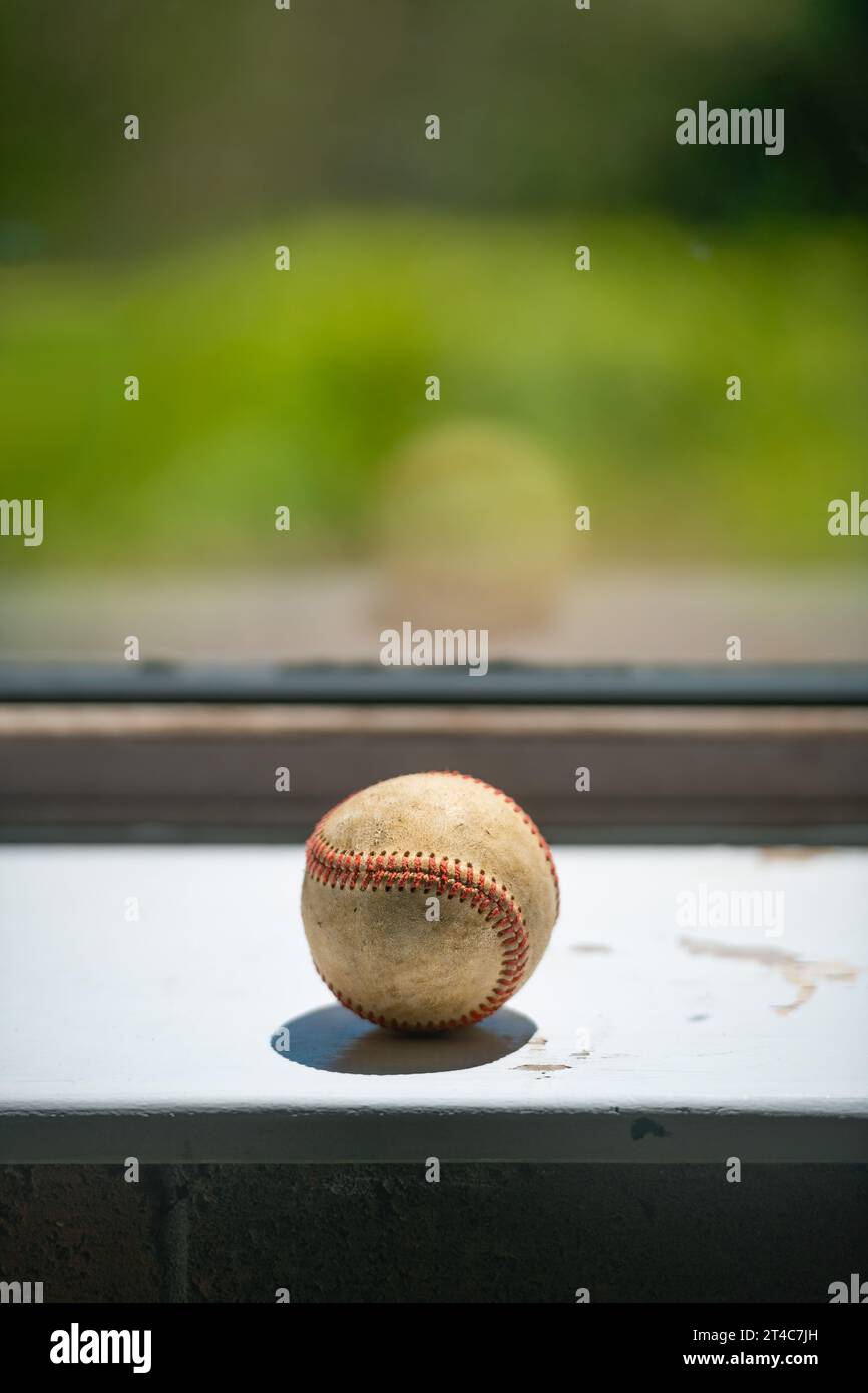 Pelota de béisbol vieja situada en la ventana sucia con espacio de copia Foto de stock