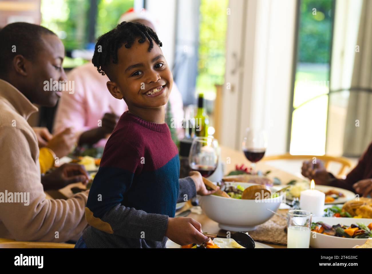 Niño afroamericano sonriendo en la cena familiar de navidad en el comedor decorado en casa Foto de stock