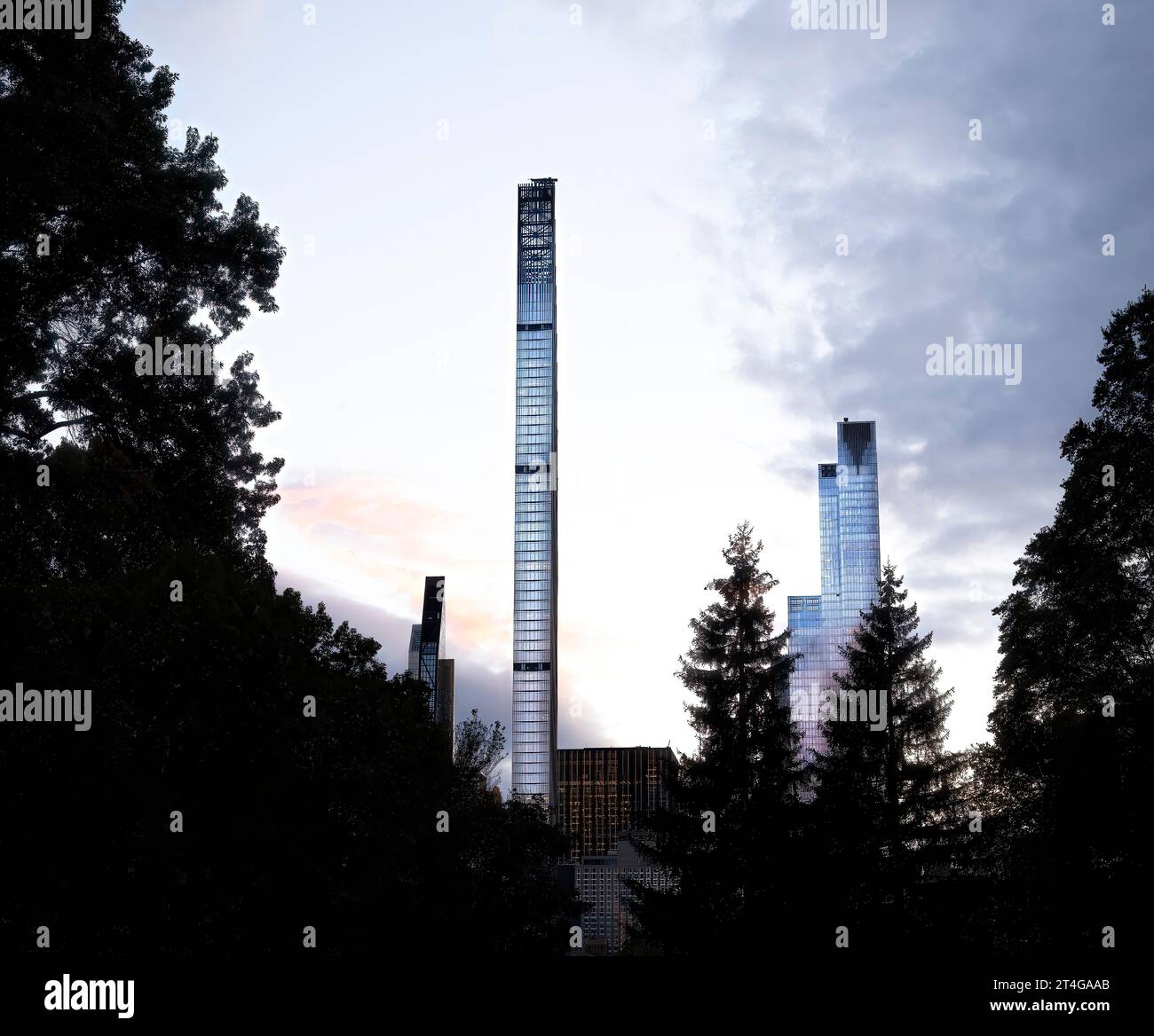 Los rascacielos de la ciudad de Nueva York brillan contra las nubes al caer la noche, vistos a través de los árboles, con la icónica torre Steinway (111 W. 57) levantándose en el centro. Foto de stock