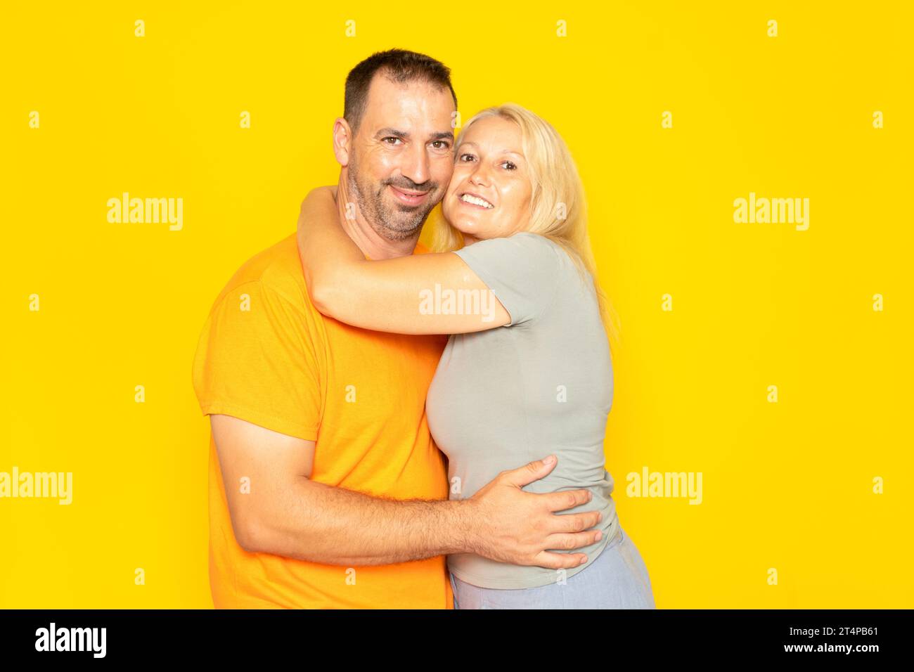 Real pareja caucásica en sus 40 años abrazándose tiernamente el uno al otro demostrando su amor y compromiso, aislado en el fondo amarillo. Foto de stock