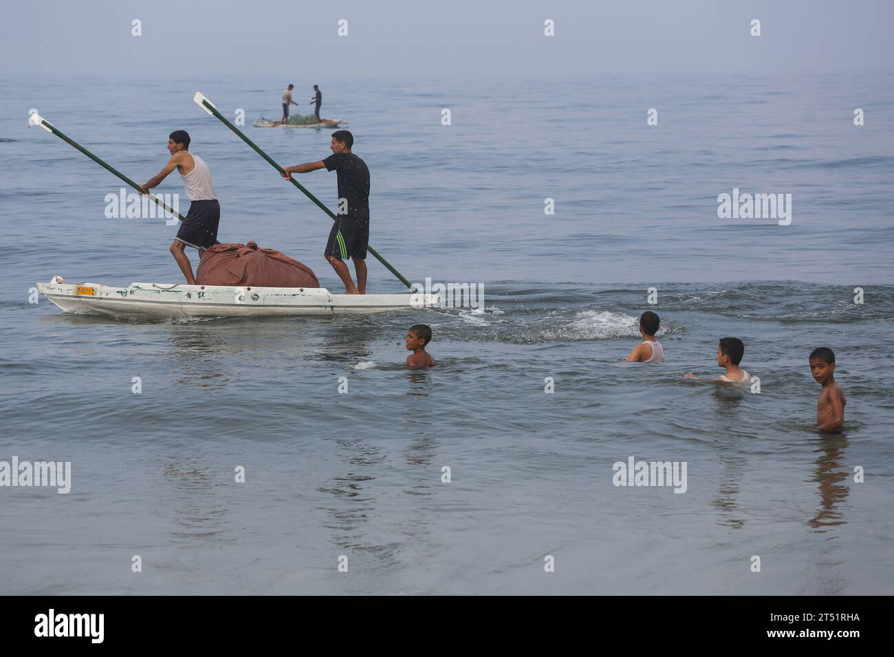 Pescadores palestinos vistos en su barco de pesca mientras los palestinos se bañan, mientras otros (no vistos) lavan su ropa y lavan los utensilios de cocina usando agua de mar debido a la falta de agua dulce y electricidad, a lo largo de la playa de Deir el-Balah en el sur de la Franja de Gaza el 2 de noviembre de 2023, en medio de las batallas en curso entre Israel y el grupo palestino Hamas. Israel golpeó Gaza, gobernada por Hamás, el 29 de octubre, en una creciente campaña aérea y terrestre, mientras la ONU advirtió que el orden civil estaba "empezando a derrumbarse" en el asediado territorio palestino. Miles de civiles, tanto palestinos como israelíes, han d Foto de stock
