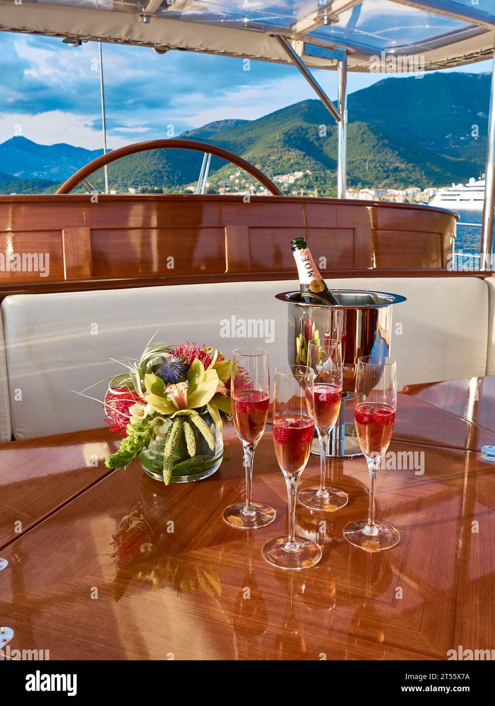 Copas de champán rosa Moet con un cubo de hielo en una hermosa mesa de teca barnizada en la cabina de un yate de vela de lujo. Foto de stock