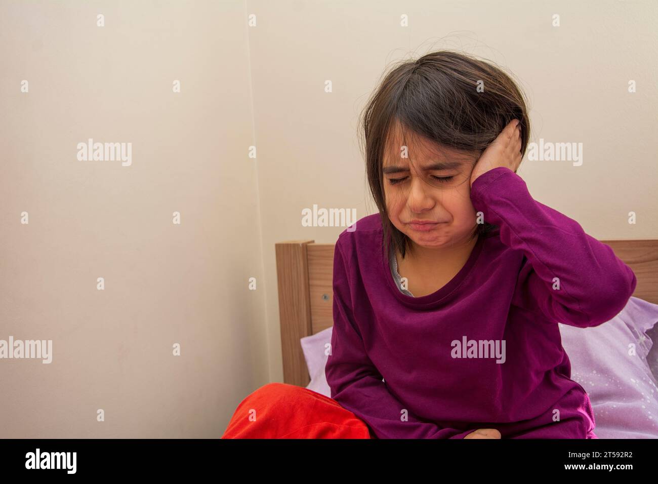 Niña en edad de la escuela primaria sentada en su cama con dolor de oído Foto de stock