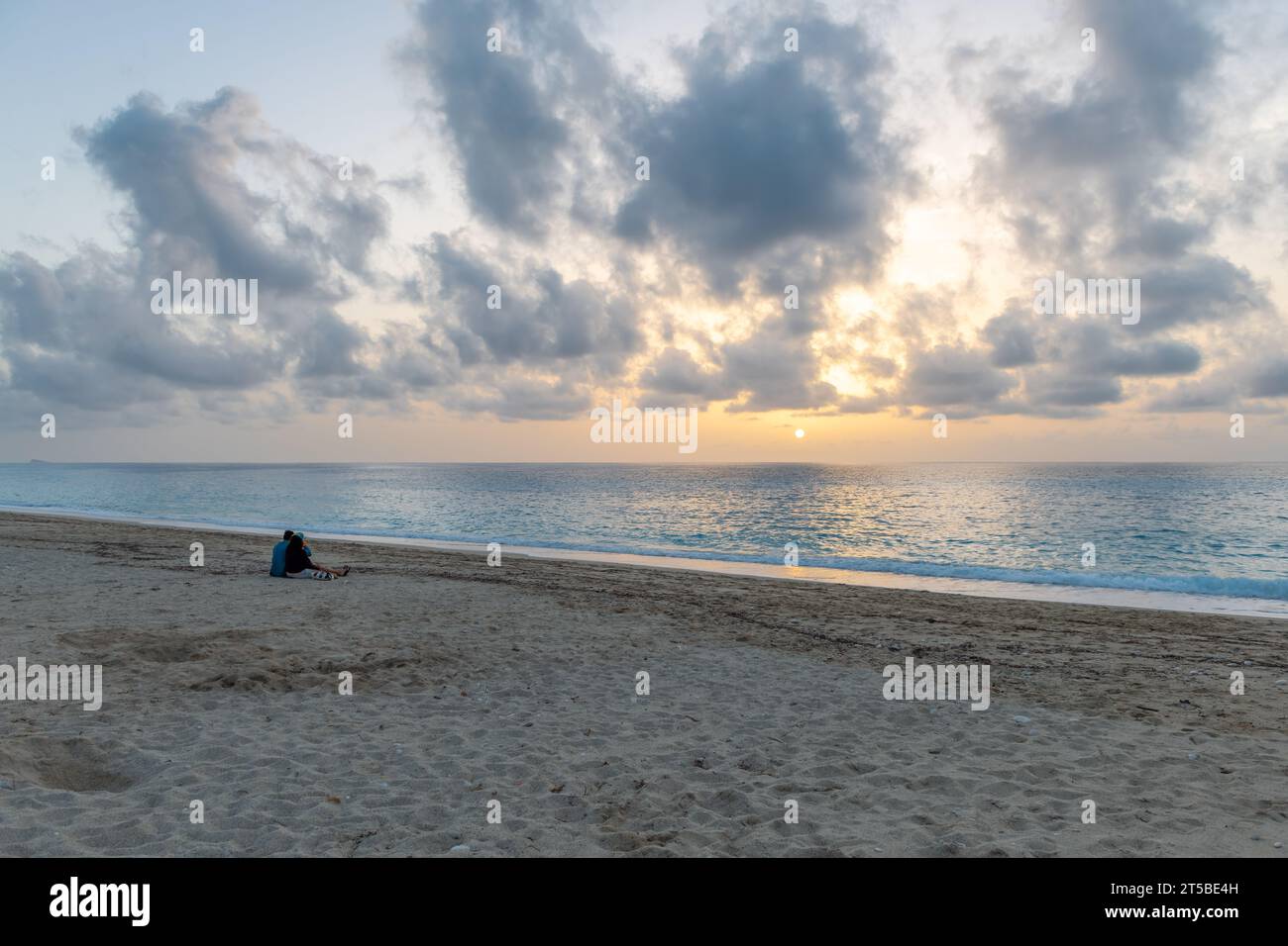 Una pareja de vacaciones sentada en una playa disfrutando de la puesta de sol. Foto de stock