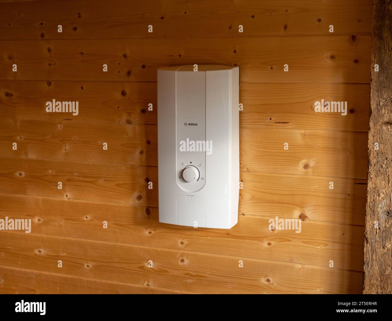 Calentador de agua Bosch en una pared interior de madera. Calentador de flujo eléctrico para obtener agua caliente para ducharse en una casa pequeña sin una caldera. Foto de stock