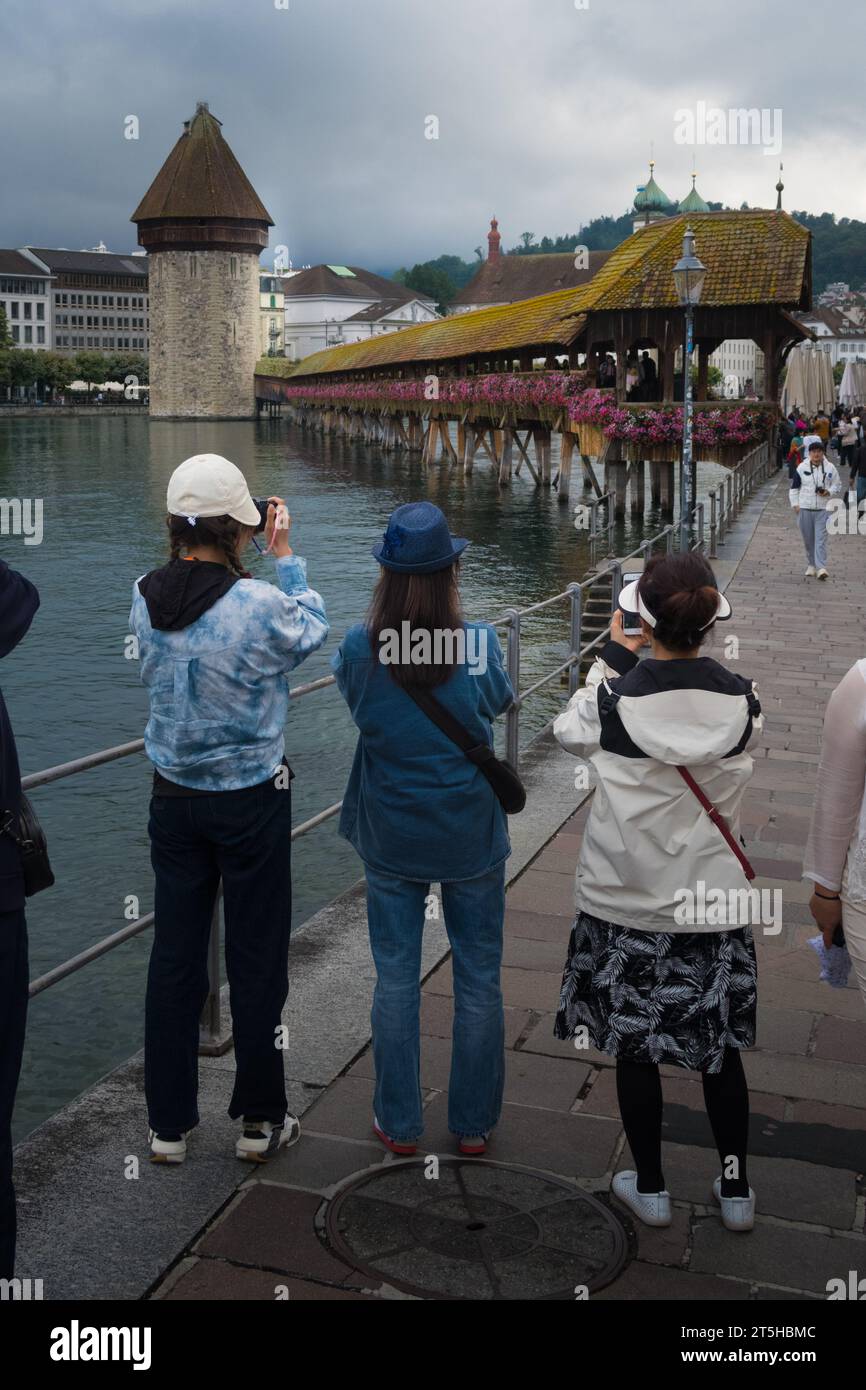 Lucerna, Suiza, 26 de agosto de 2023 - Los turistas asiáticos toman fotos y selfies bajo la lluvia frente al puente de la Capilla Foto de stock