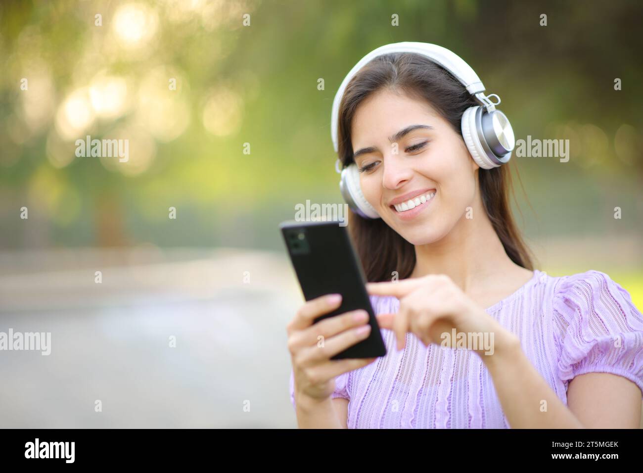 Mujer feliz escuchando música usando auriculares y teléfono inteligente en un parque Foto de stock