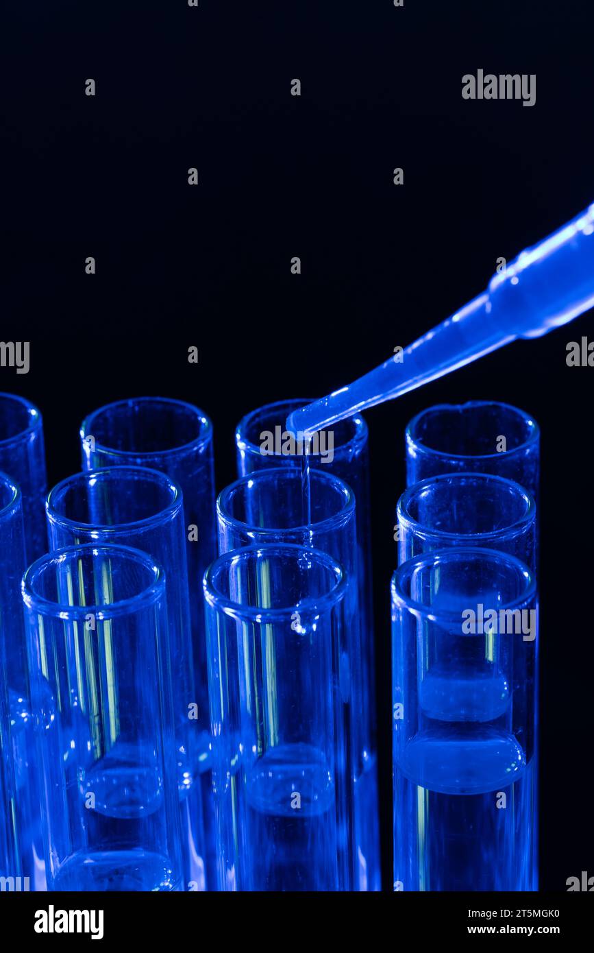 Imagen vertical de cerca de tubos de ensayo de laboratorio y pipeta con espacio de copia sobre fondo negro Foto de stock
