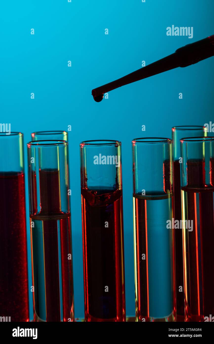 Imagen vertical de cerca de tubos de prueba de laboratorio y pipeta con espacio de copia sobre fondo azul Foto de stock