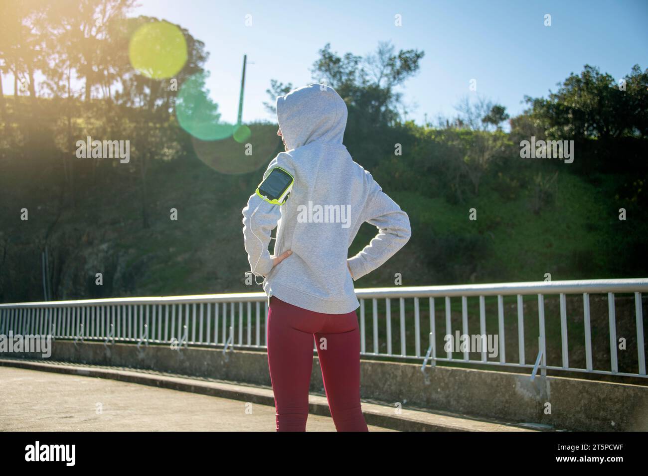 corredor deportivo de mujer que lleva una sudadera con capucha y auriculares de pie descansando con las manos en las caderas. Foto de stock