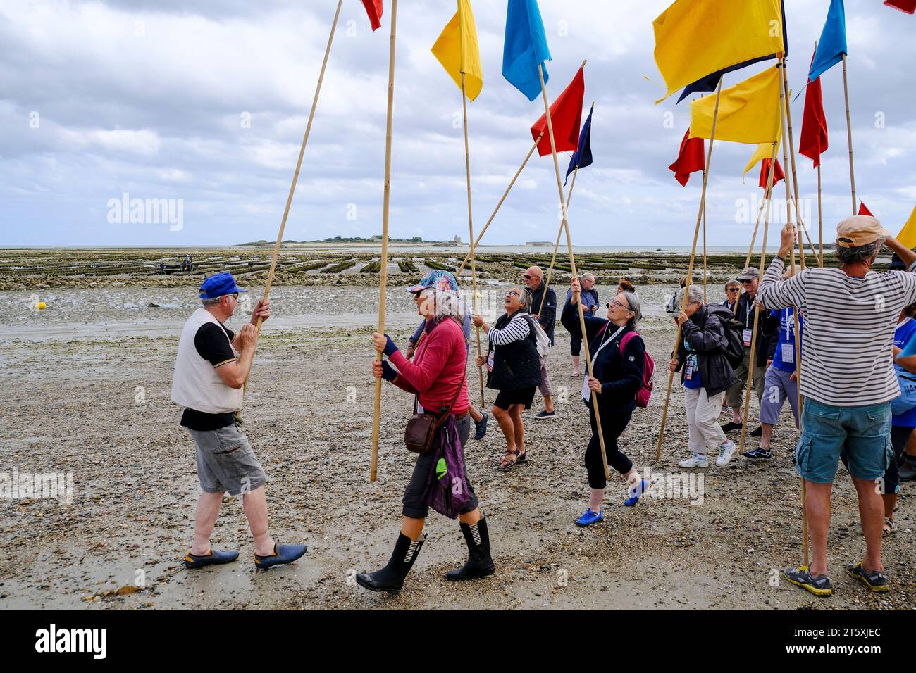 Frankreich, Saint-Vaast-la-Hougue, 30.08.2023: Einheimische und Touristinnen sammeln sich mit bunten Fahnen und Wimpeln am Strand für die Grande Trave Foto de stock