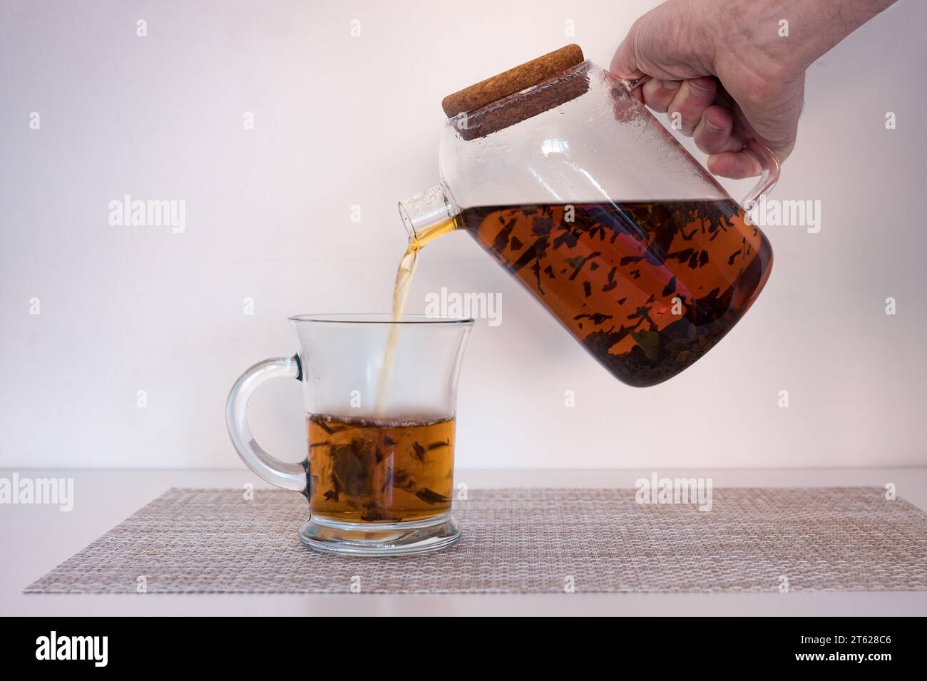 Agua caliente vertiendo en una taza de cristal de la tetera con las hojas de té negro o rojo en ella. Foto de stock