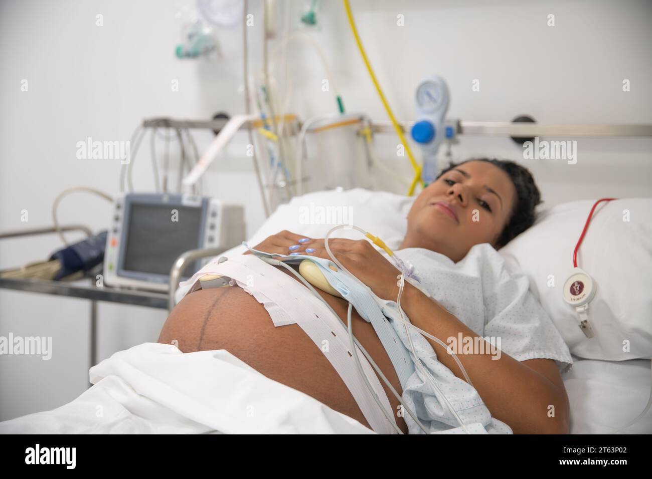 Primer plano de una mujer embarazada serena que descansa en una cama de hospital, conectada a dispositivos médicos, enfatizando la paz y la confianza en la atención médica Foto de stock