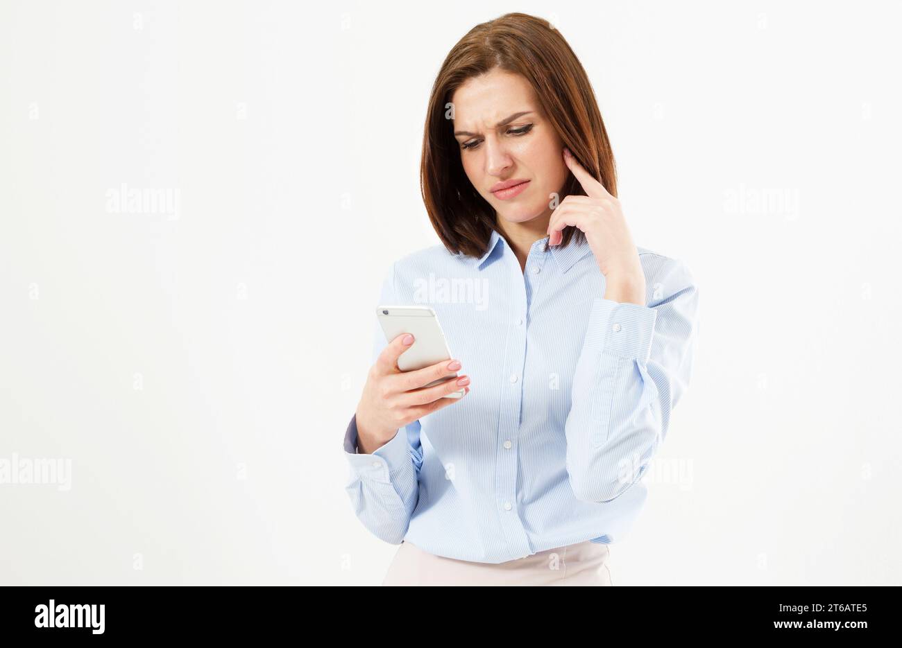 Mujer molesta sosteniendo un teléfono celular. Joven empresaria enojada leyendo malas noticias en su teléfono celular. Aislado sobre fondo blanco. Foto de stock