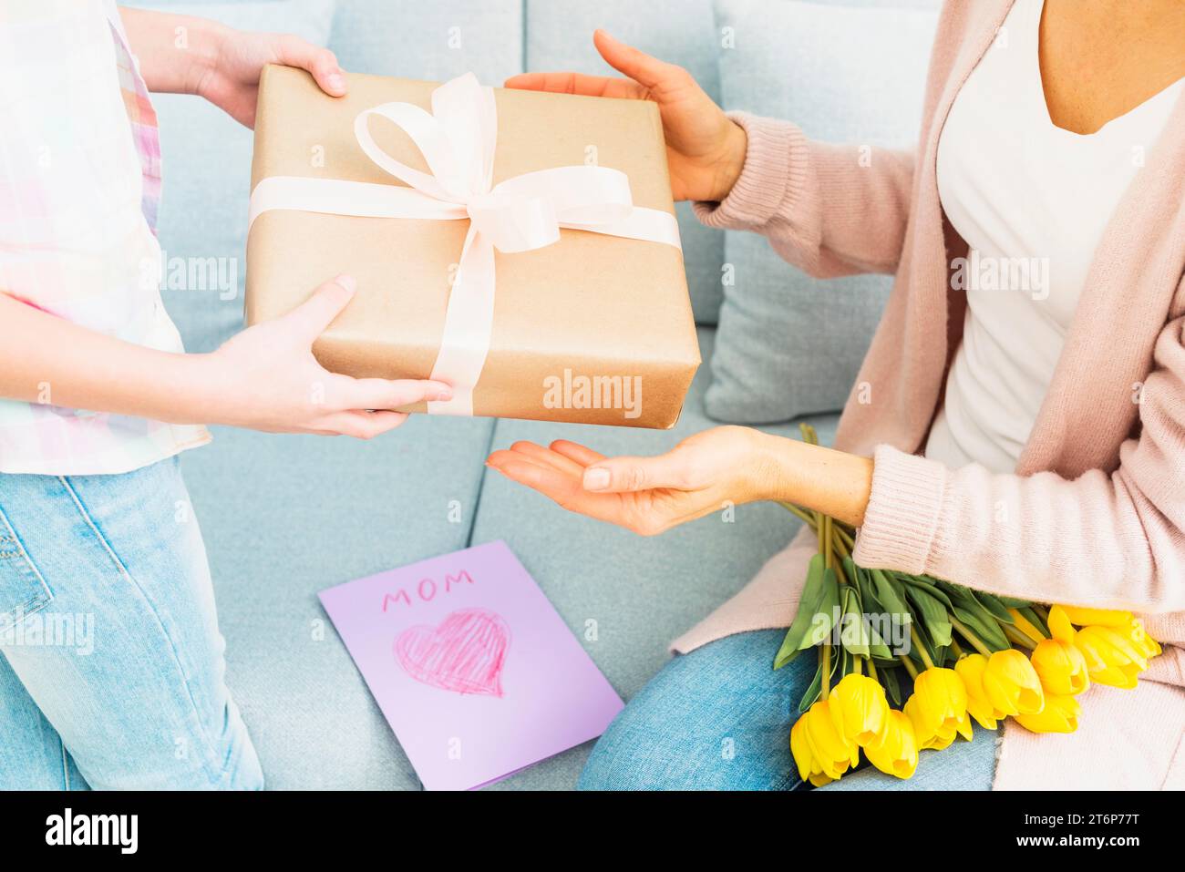 La niña le da a su mamá una caja de regalo y un ramo de flores de