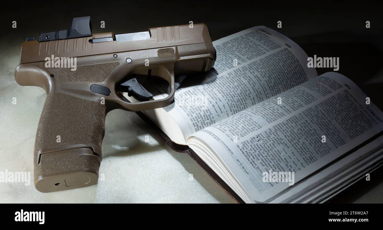 Pistola automática con la santa Biblia abierta a la sección del libro de Lucas en la que Jesús les dijo a sus discípulos que compraran una espada. Foto de stock