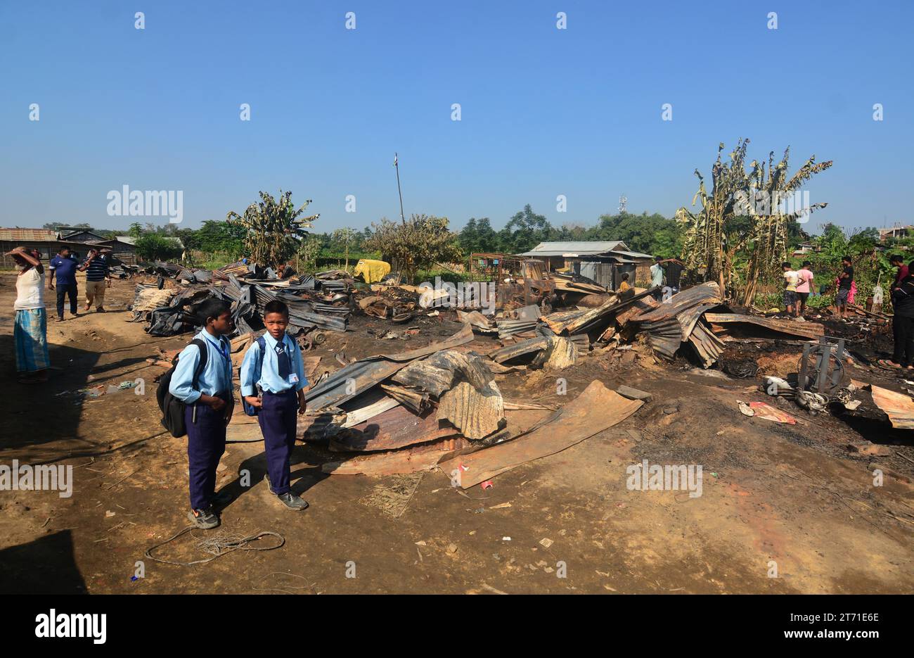 Dimapur, India: 13 de noviembre de 2023: Paso de estudiantes de escuela entre casa carbonizada después de un infierno en la noche de Diwali, la celebración del Festival Hindú de la Luz, que destruyó al menos 50 casas matando a 5 personas en Naharbari en Dimapur, India, estado nororiental de Nagaland. Crédito: Caisii Mao/Alamy Live News Foto de stock