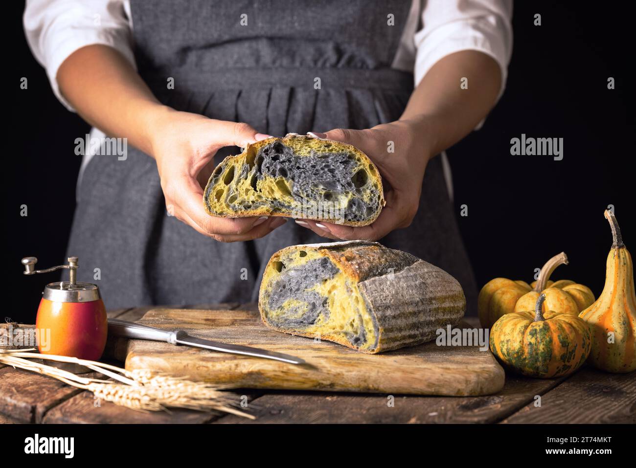 Masa madre casera activado carbón negro pan con calabaza horno de cúrcuma al horno y ama de casa mujer panadero con comida de temporada de otoño, viejo rústico Foto de stock