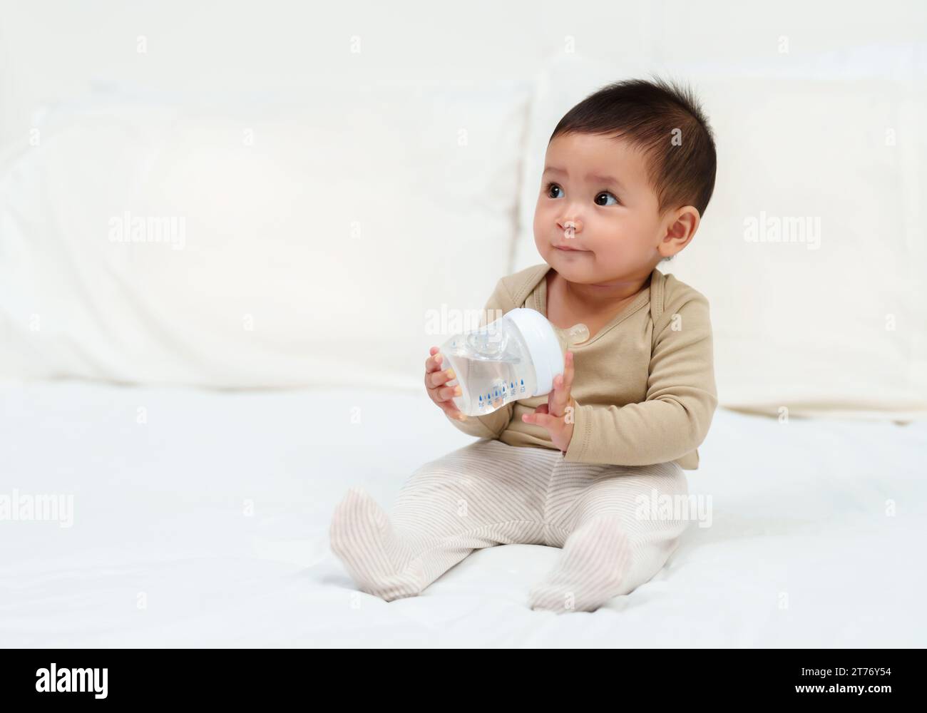 Bebé de 6 meses bebe agua de un biberón, acostado en la cama. bebe feliz y  alegre