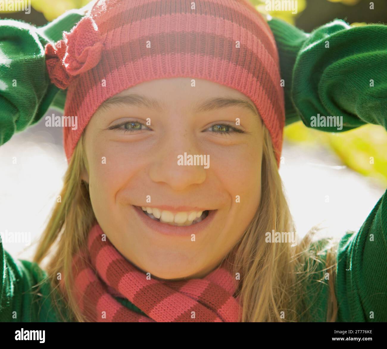 Chica joven sonriente con las manos en la cabeza con un sombrero lanudo Foto de stock