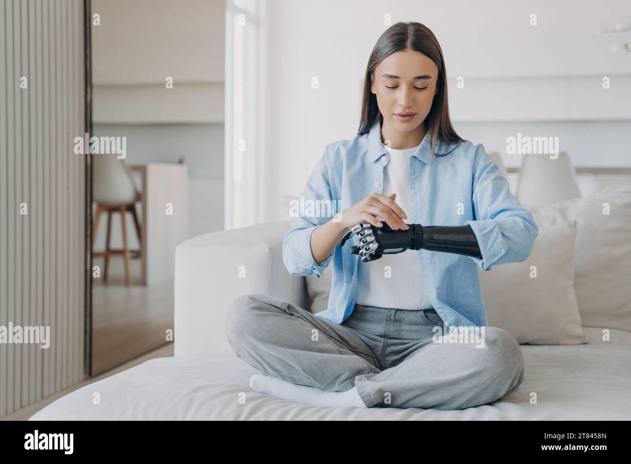 Mujer joven serena en meditación con un brazo biónico, mezclando tranquilidad con tecnología en un entorno moderno Foto de stock