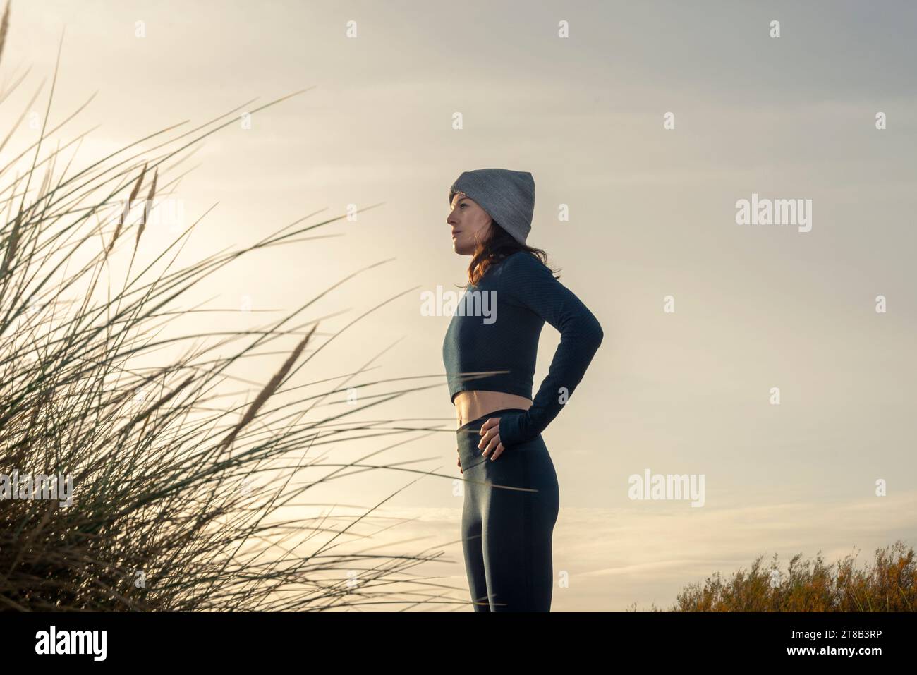 vista lateral de una mujer deportiva con las manos en las caderas descansando después de hacer ejercicio al aire libre, otoño, invierno serie de fitness. Foto de stock