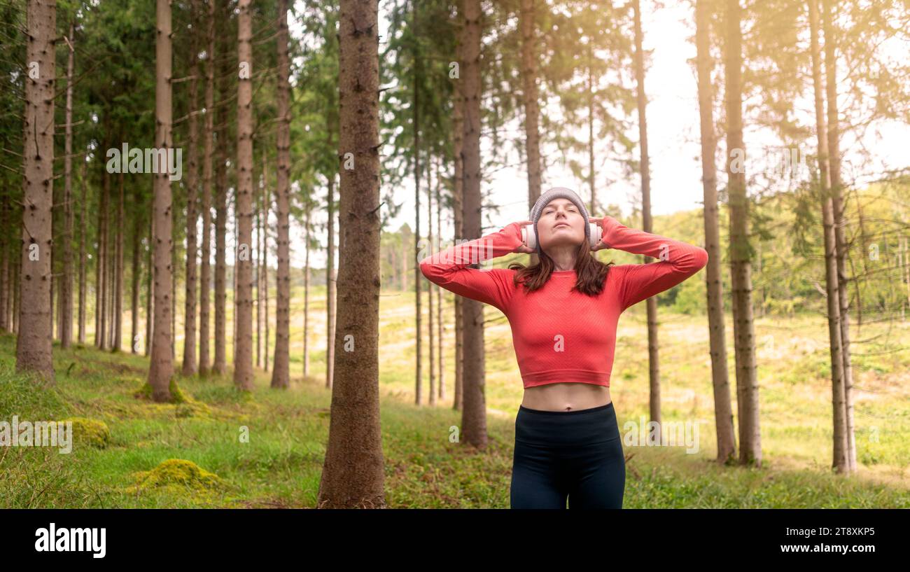Mujer deportiva corredor entrenando al aire libre en un bosque, escuchando música con auriculares Foto de stock