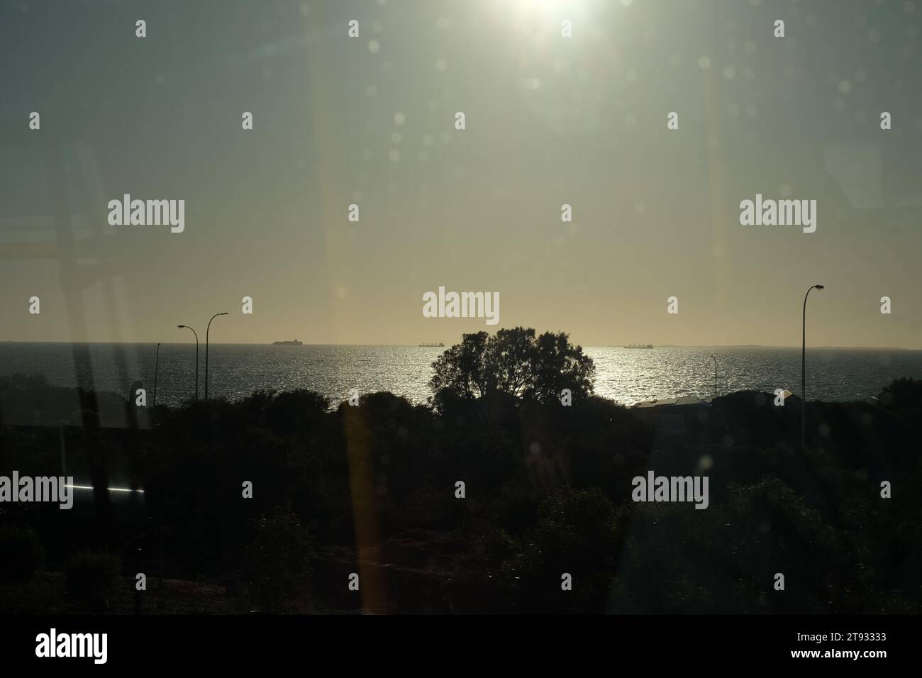 Vista de la ventana desde un tren, el sol sobre el Océano Índico, pequeños barcos en el horizonte, un paisaje en silueta a través de vidrios tintados, manchas de reflejos Foto de stock