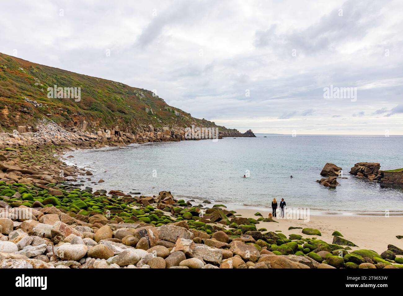 Lamorna Cove, dos personas paseando a su perro en la playa de arena, Cornualles suroeste de Inglaterra, Reino Unido, 2023 Foto de stock