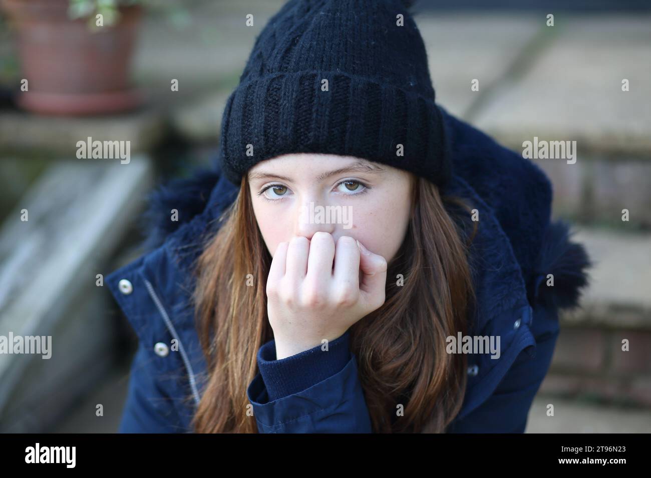 Chica sentada en el paso con sombrero de lana y abrigo y bufanda tratando de mantener el calor Foto de stock