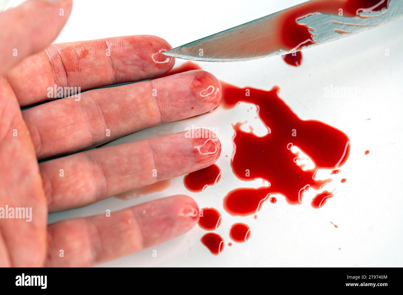 Primer plano del brazo en charco sangriento y cuchillo con sangre en la superficie blanca, cuadro conceptual sobre el suicidio y el asesinato Foto de stock