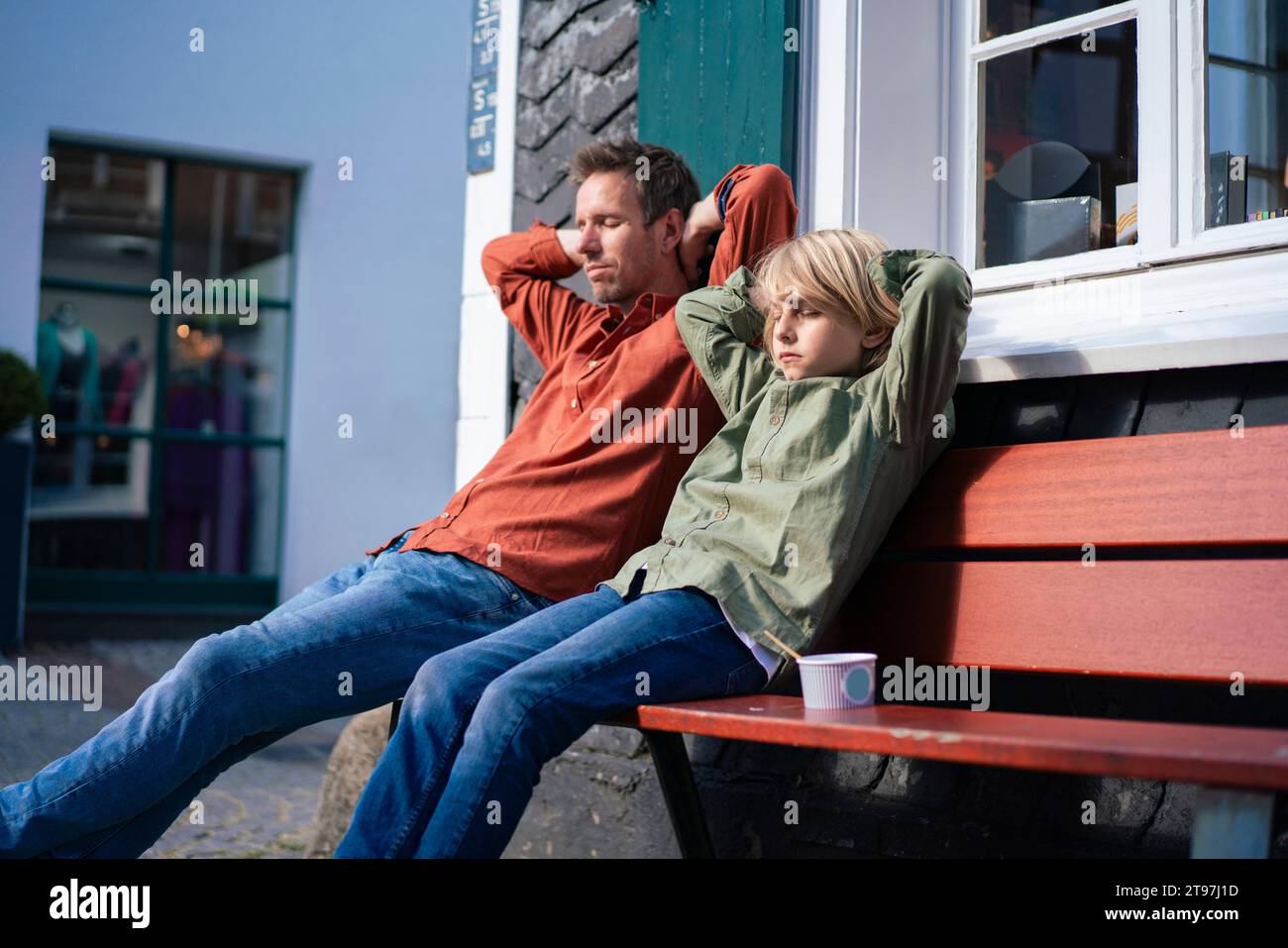 Padre e hijo con las manos detrás de la cabeza sentados en el banco Foto de stock