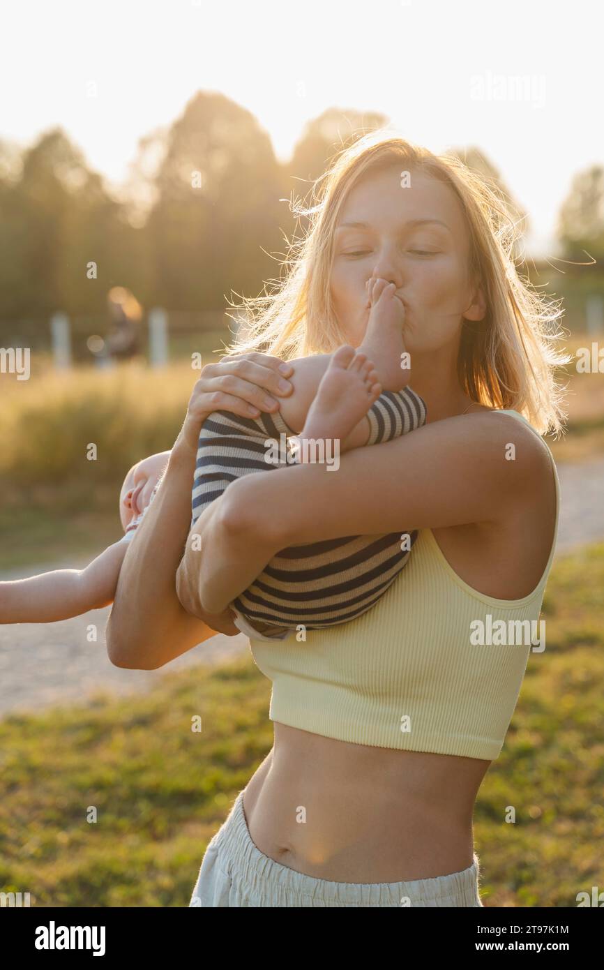 Madre amorosa besando el pie del bebé en el parque al atardecer Foto de stock