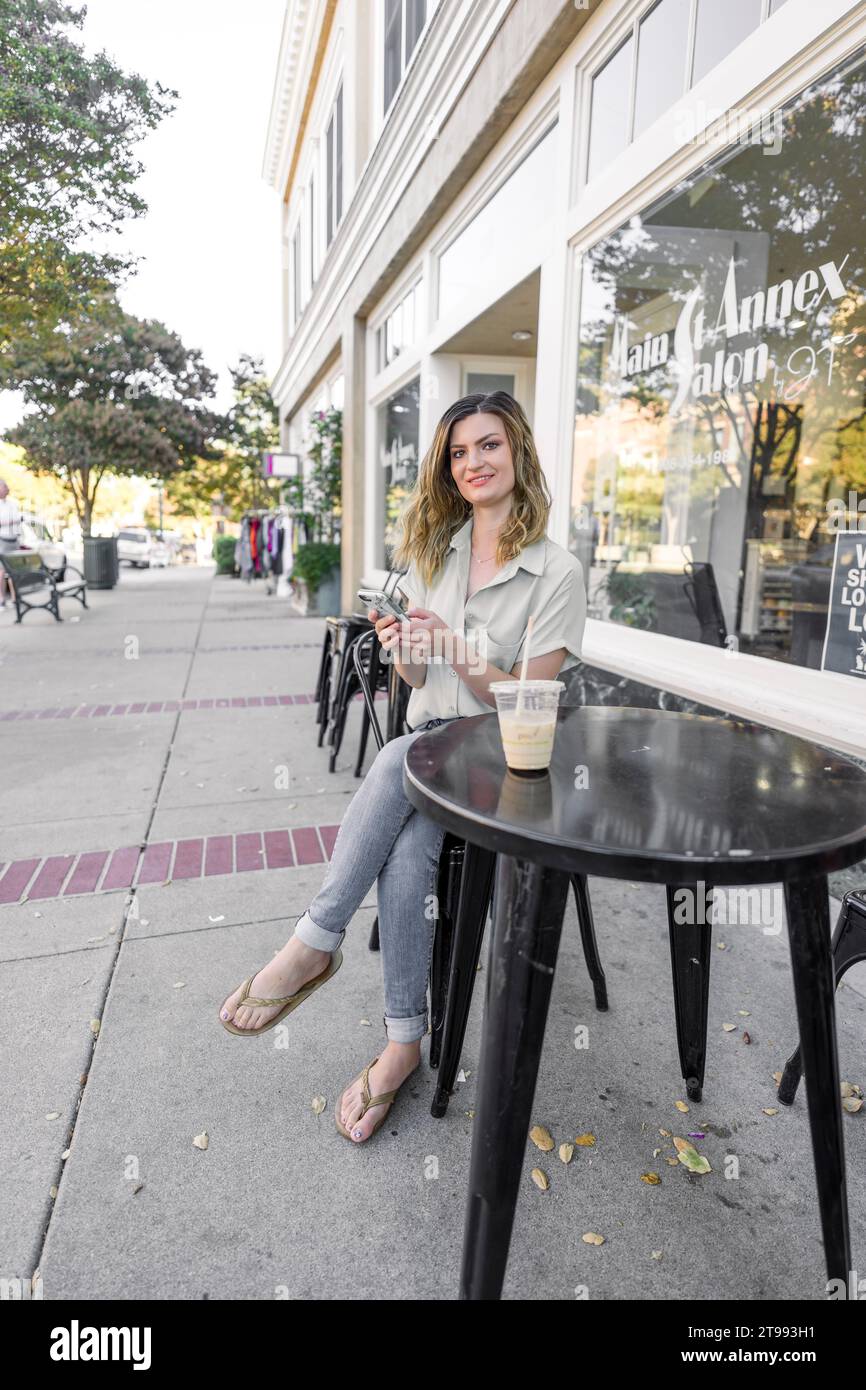 Hermosa mujer joven sentada con un café helado en una acera Café Downtown Foto de stock