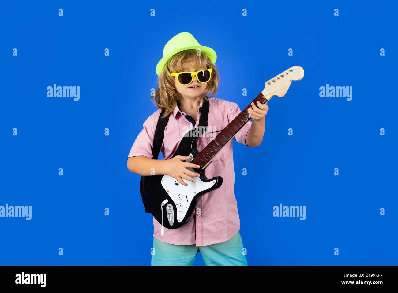 Niño músico tocando la guitarra como una estrella de rock sobre fondo azul en estudio. Niño tocando la guitarra como una estrella de rock Foto de stock