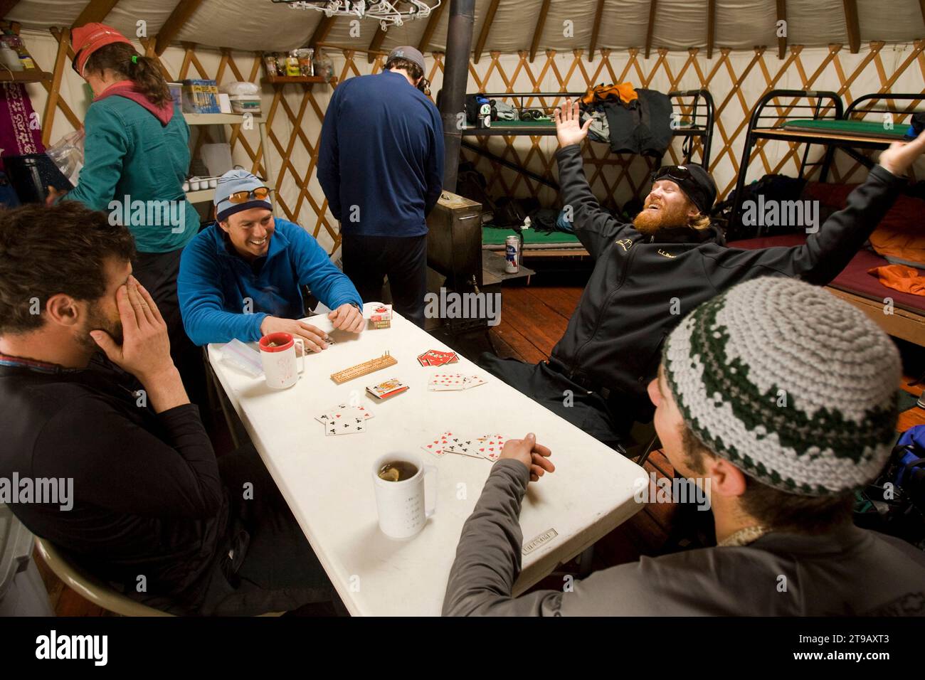 Grupo de amigos riendo y jugando a las cartas en una yurta de invierno. Foto de stock