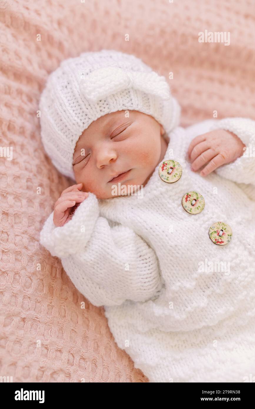 Bebé recién nacido con gorro de punto blanco y un par de zapatos blancos y  rosados.