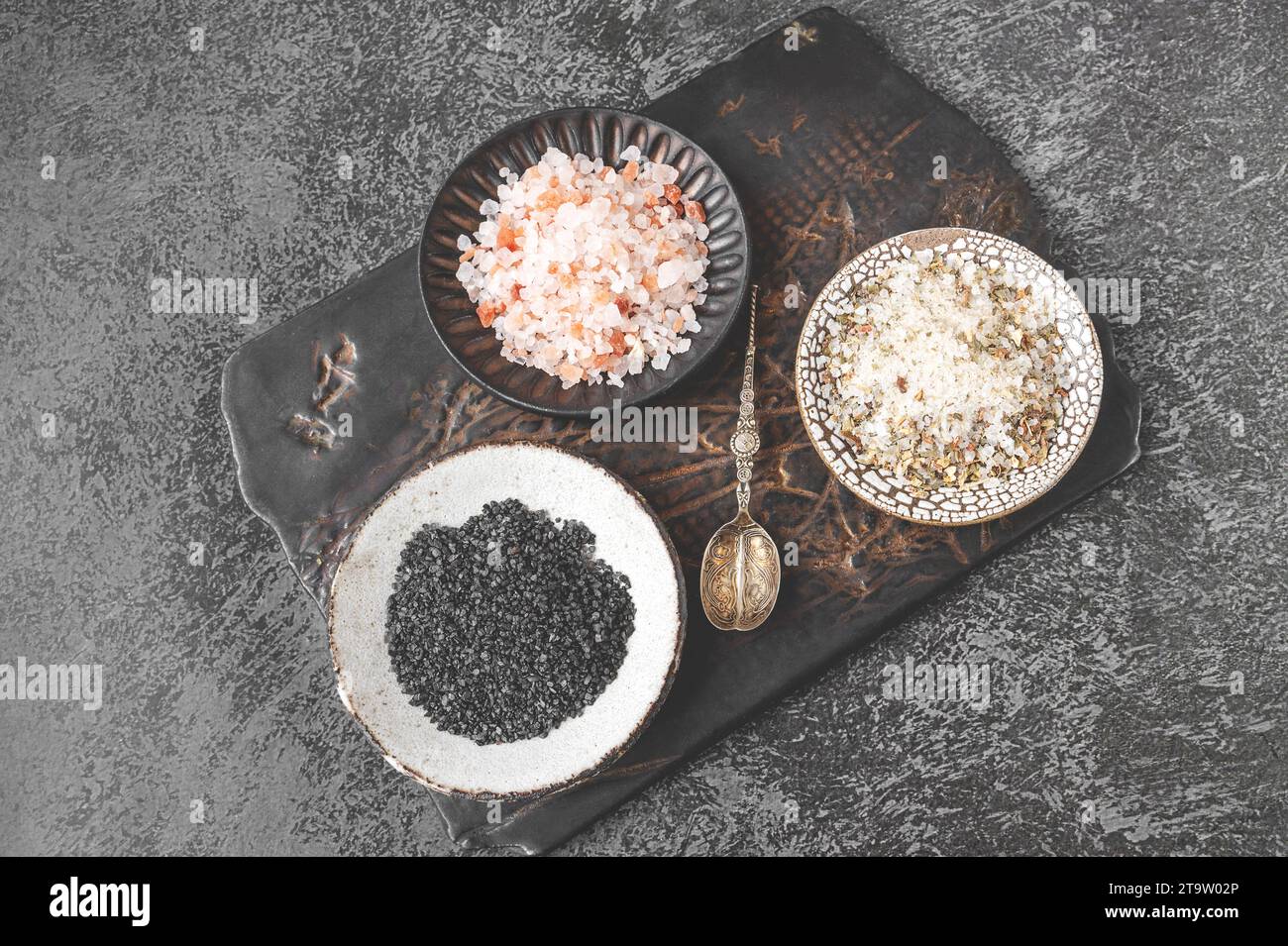 Diferentes tipos de sal: Rosa del Himalaya, negro y sal especiada en una placa kraft hecha a mano en una tabla de cortar de arcilla. Vista superior. Foto de stock