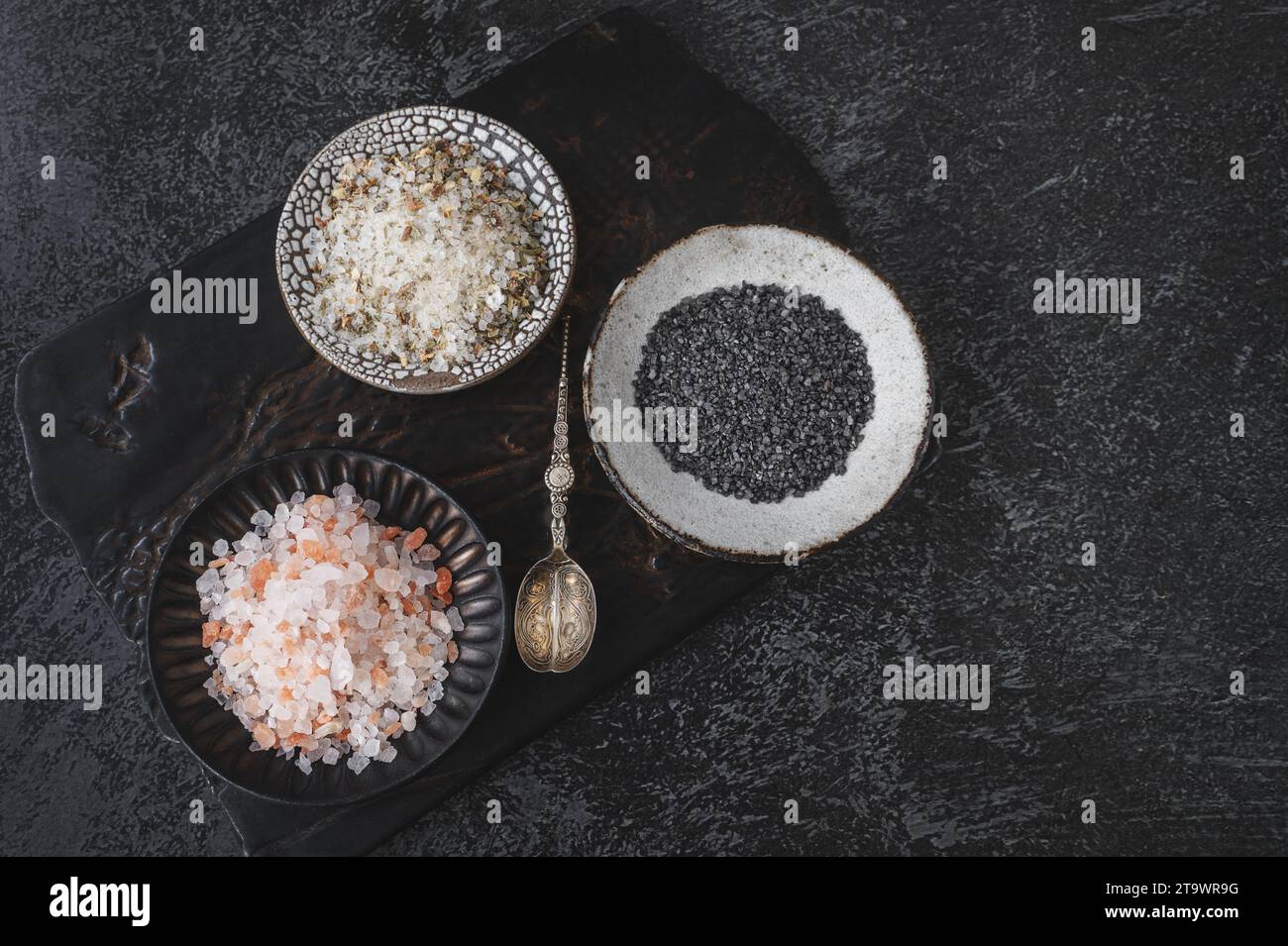 Diferentes tipos de sal: Rosa del Himalaya, negro y sal especiada en una placa kraft hecha a mano en una tabla de cortar de arcilla. Vista superior. Copiar espacio Foto de stock