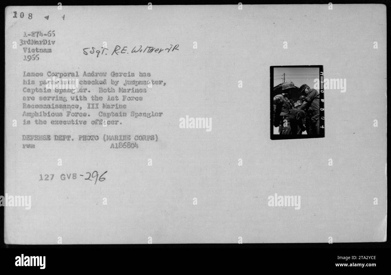 Leyenda: El cabo Andrew García, de la Fuerza de Reconocimiento de la Marina, tiene su paracaídas revisado por el capitán Spangler durante una misión de reconocimiento en Vietnam en 1966. El Capitán Spangler, que sirve como oficial ejecutivo, garantiza la seguridad y la preparación de sus infantes de marina. Esta imagen fue capturada por el Departamento de Defensa (Cuerpo de Infantería de Marina de EE.UU.) y catalogada como A18680 Yum 127 GVB-296 C. Foto de stock