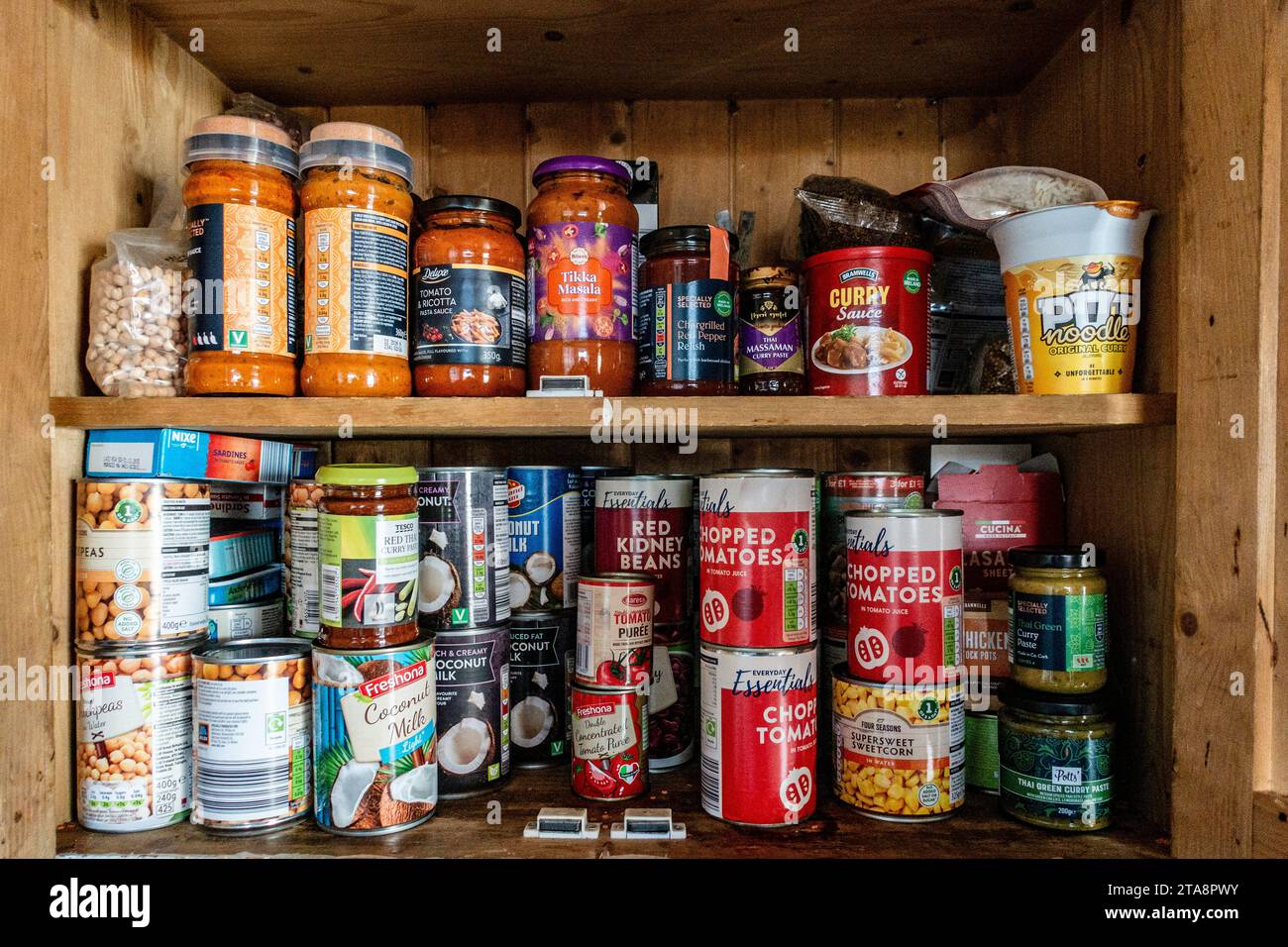 Organización de la mujer de la despensa en la cocina cerca del estante de  madera con latas y recipientes de comida.